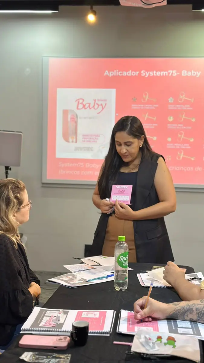 Instrutora realizando a entrega de certificado de conclusão profissional para aluna nas dependências do curso perfuração de orelha