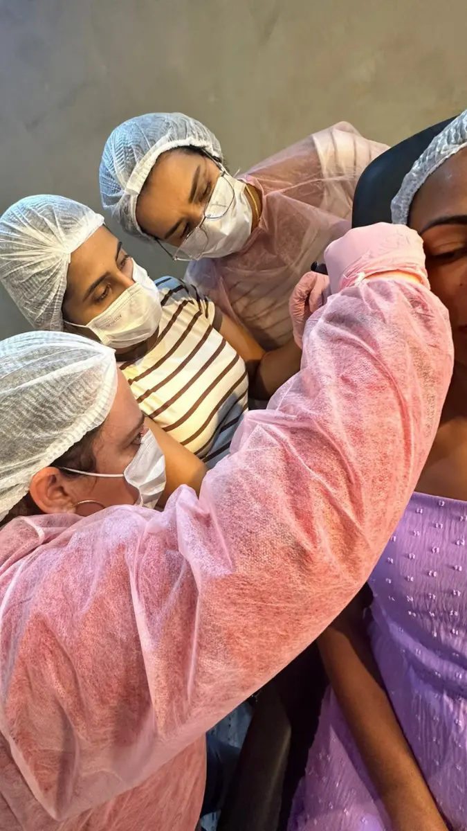 Duas profissionais de saúde utilizando uniformes e máscaras protetoras durante atividade prática do curso de perfuração de orelha